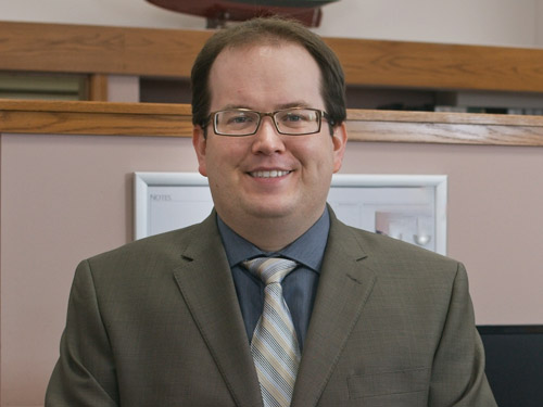 Young dark haired probate lawyer Sean Nichols standing up wearing a brown suit
