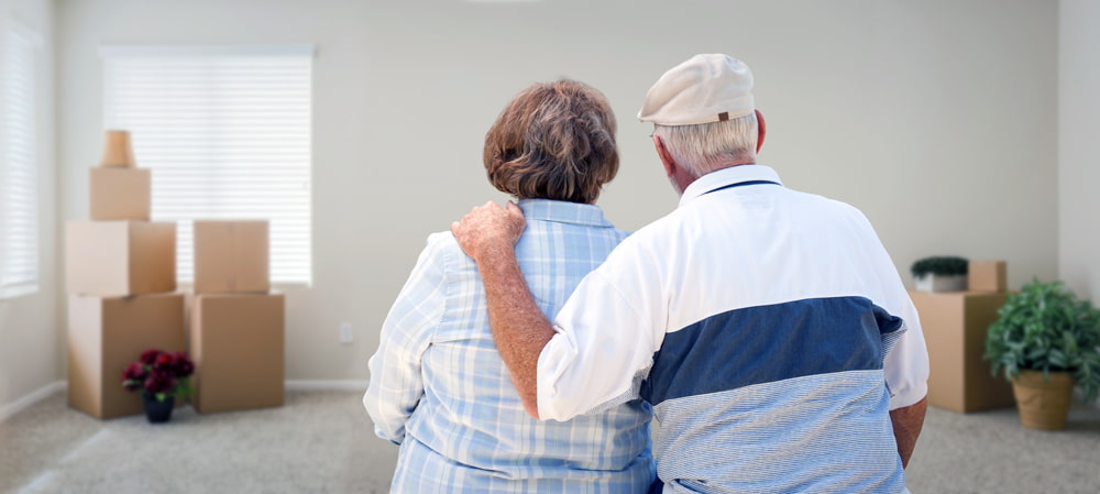 An elderly couple comforting each other in a empty room with moving boxes